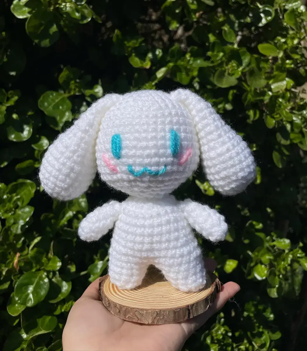 Cinnamoroll blanco tejido sostenido sobre una base de madera