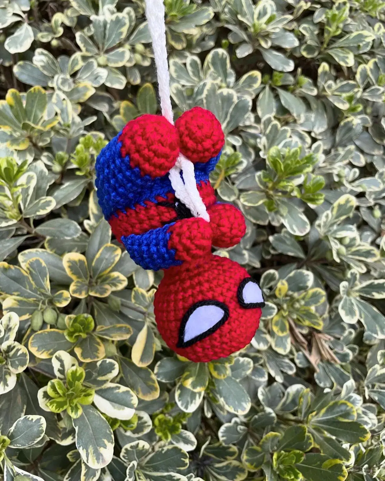 Amigurumi de Spiderman colgando cabeza abajo de un cordón blanco